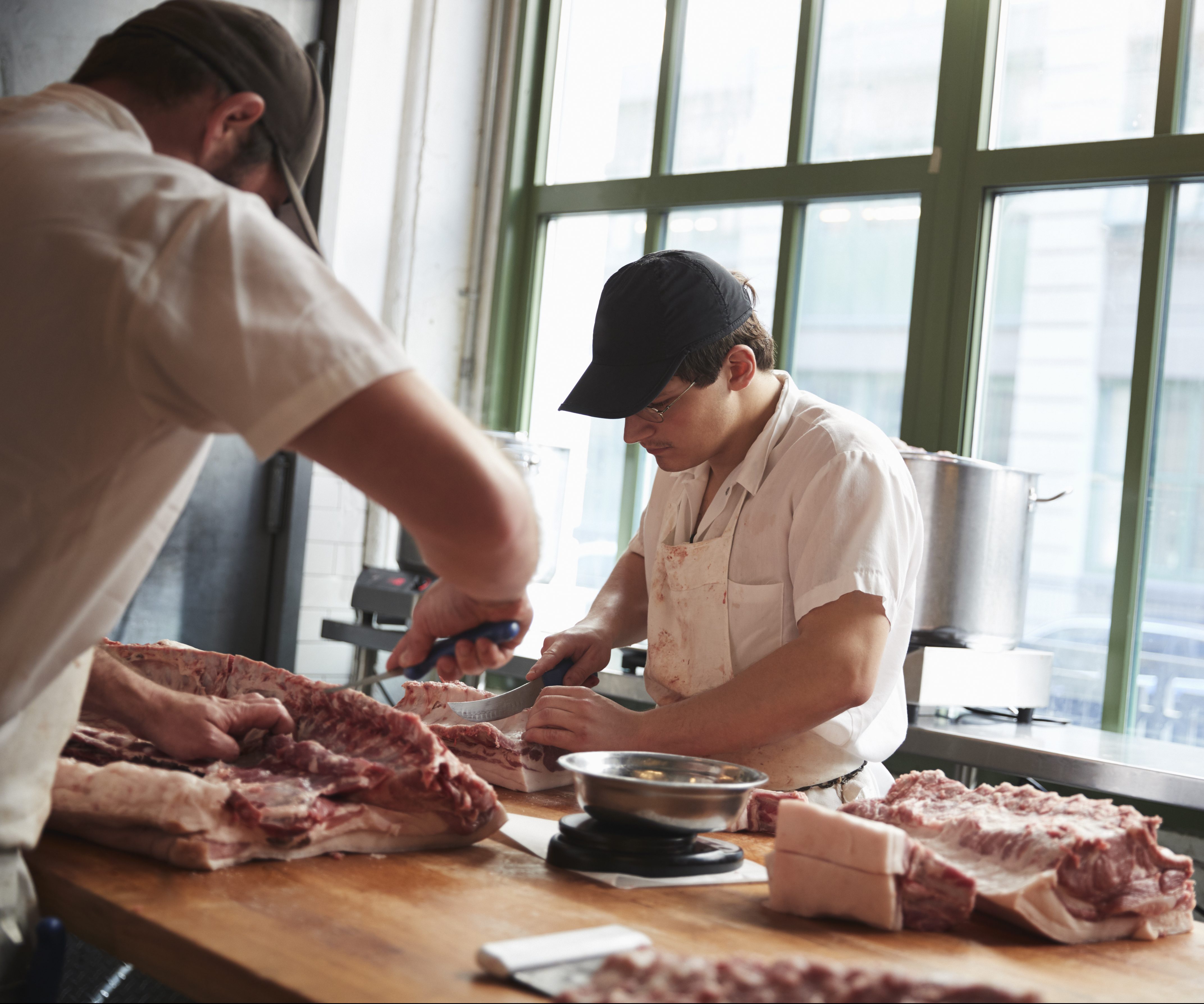 Two butchers cutting meat to sell at a butcher’s shop